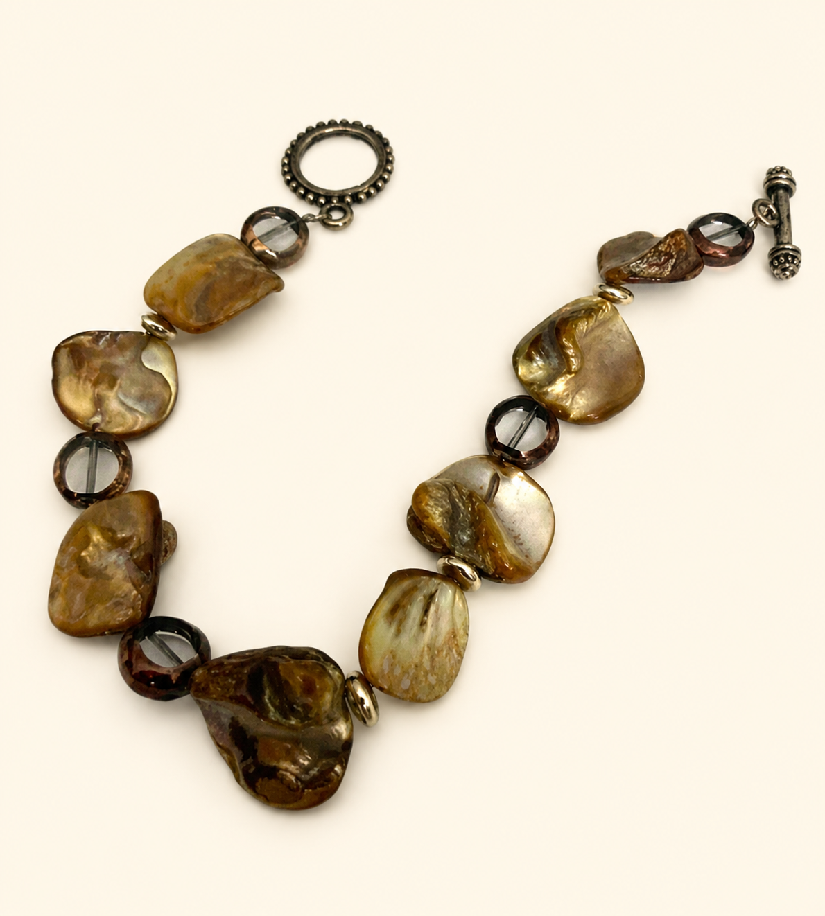 A beaded statement necklace featuring irregular polished brown and gold-toned stones, dark brown translucent beads, and antique silver-tone clasp hardware on a light cream background.