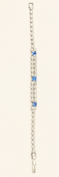 A silver-toned tennis bracelet featuring three small blue gemstone accents spaced along the center, set against a plain off-white background.