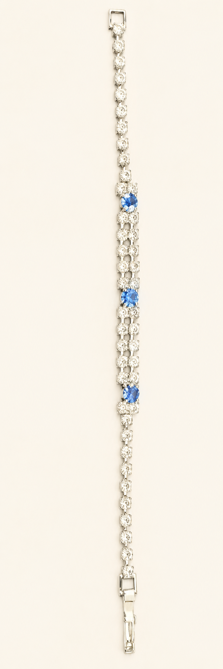 A silver-toned tennis bracelet featuring three small blue gemstone accents spaced along the center, set against a plain off-white background.