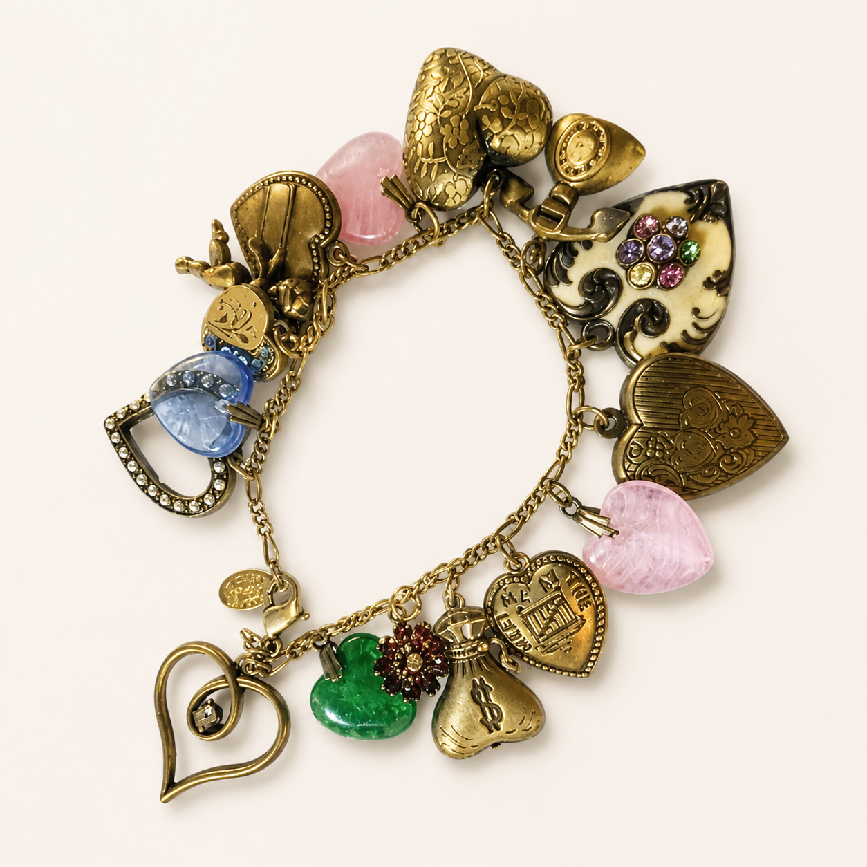 A vintage-style charm bracelet with multiple heart and decorative charms, including gold-toned hearts, pink stone accents, a blue gem, and a small floral charm, displayed on a light cream background.