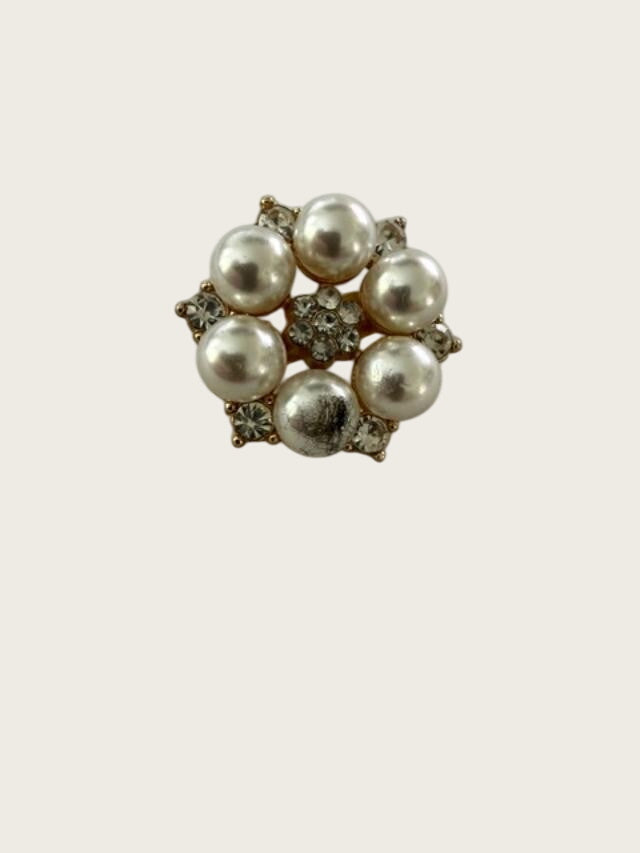 A vintage-style floral brooch featuring five white pearls and small clear rhinestones in a gold-tone setting, displayed on a textured light gray surface.