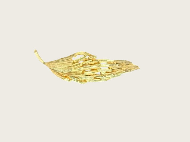 A gold-toned leaf-shaped brooch with a textured, layered design, displayed on a black velvet surface.