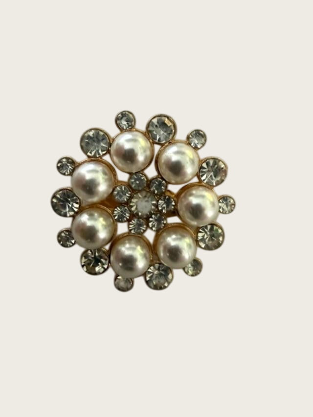 A vintage-style floral brooch featuring large cream-colored faux pearls and clear rhinestones in a gold-tone setting, displayed on a textured white surface.